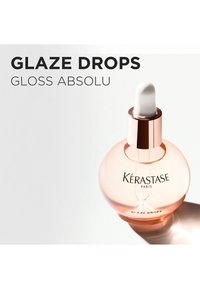 Kérastase Glaze Drops en un frasco redondo transparente de color rosa con tapa de gotero blanca; presenta el logo de la marca y el nombre del producto en tipografía elegante.