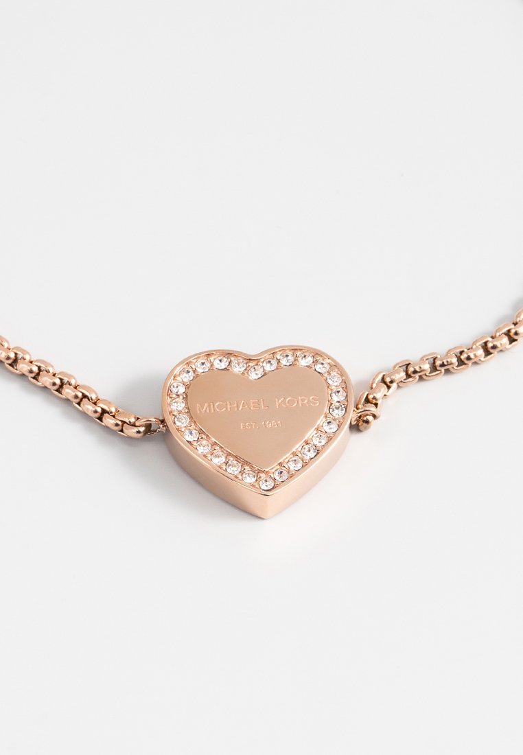 Collana a pendente a forma di cuore in oro rosa con accenti di cristallo. Il design della catena presenta sezioni collegate tra loro. Incisioni "Michael Kors" e "EST. 1981."