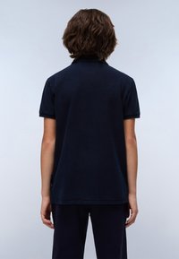 Mörkblå pikétröja i texturerat tyg, med klassisk krage och korta ärmar, med en diskret logotypdetalj på sidan.