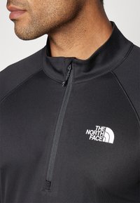 Zwarte zip-up jack met hoge kraag, gestructureerde stof en wit logo van The North Face op de linkerborst.