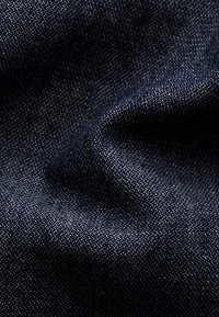 Ciemnoniebieski denimu materiał o gładkiej teksturze, z subtelnym wzorem wełnianym i lekkim połyskiem. Zmarszczki podkreślają jego miękkie układanie.