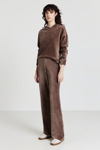 Felpa con cappuccio in velluto a coste marrone e pantaloni a gamba larga abbinati. Tessuto morbido con motivo a coste. Modello che indossa sneakers bianche con suola marrone.