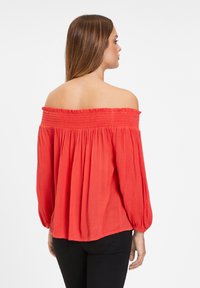 Blusa roja sin mangas con cuello elástico fruncido, mangas largas abullonadas y un corte holgado, con un tejido texturizado.