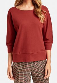Rostfarbener, leichter Pullover mit weitem Ausschnitt und Dreiviertelärmeln. Er verfügt über einen lockeren Schnitt und eine horizontale Naht am Saum.