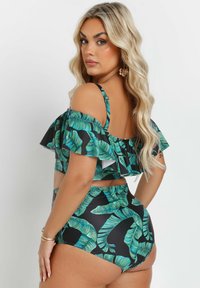 Svart tvådelad baddräkt med grönt mönster av bananblad, rynkad topp med avskurna axelremmar och högmidjade byxor.