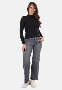 Maglietta nera a maniche lunghe con un alto collo, abbinata a jeans dritti blu sbiaditi e sneakers bianche. Design semplice e minimalista.