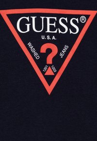 Black cotton T-shirt with red triangle logo. "GUESS® U.S.A." displayed prominently, with "WASHED" and "JEANS" text surrounding a question mark.