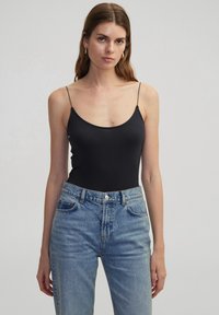 Zwart slim-fit bodysuit met dunne bandjes en een ronde halslijn. Gecombineerd met hoogwakende lichtblauwe jeans, wat een casual uitstraling geeft.