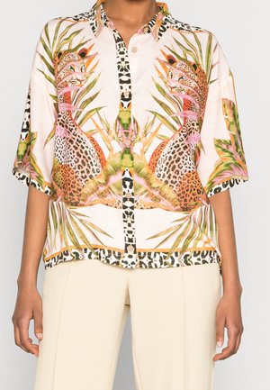 Overhemd met knopen en symmetrische print van luipaard en tropische bladeren in oranje, groene en roze tinten, gedragen met lichtbeige broek.