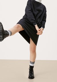 Vestido sudadera negro con mangas largas y dobladillo asimétrico. Se lleva con botas de combate negras y calcetas blancas hasta la rodilla con rayas negras.