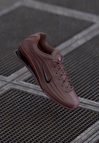 Juoksukengät Nike syvänpunaisessa sävyssä, jossa on teksturoitu päällinen, musta swoosh-logo ja pehmustettu pohja näkyvillä ilmataskuilla tuen tarjoamiseksi.