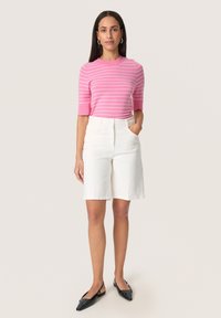 Vaaleanpunaisella ja valkoisella raidallisella lyhythihaisella neuleella, yhdistettynä valkoisiin keskipitkiin shortseihin. Slim fit -muotoilu, klassinen malli ja sileä rakenne. Mustat matalat kengät.