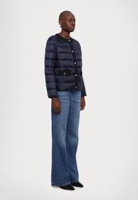 Navy puffer jacket with horizontal quilted texture, black trim, and silver buttons. Paired with wide-leg denim jeans and black pointed shoes.
