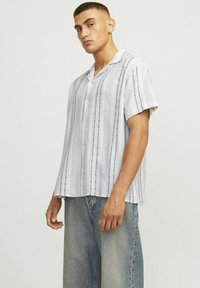 Chemise à manches courtes, avec col, de couleur gris clair, ornée de rayures noires verticales et de détails brodés subtils. Fabriquée en tissu léger.