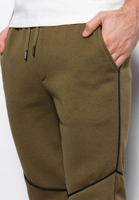 Olivgrüne Jogginghosen aus weichem Stoff, mit schwarzer Seitenpaspelierung, Kordelzugbund und Seitentaschen für Funktionalität.