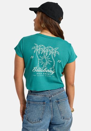 Teal kortärmad t-shirt med ribbad textur; vit tryckt palmträd och text på baksidan. Matchad med högmidjade blå denimjeans. Svart keps på huvudet.
