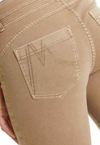 Beige denim jeans met een gestikt achterzak met een gestileerd 'V'-ontwerp. Glad textuur en een getailleerde pasvorm zichtbaar.