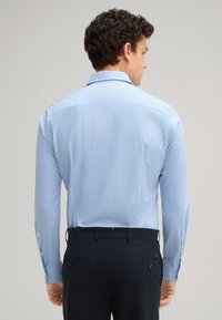 Lichtblauw overhemd met lange mouwen en een subtiel ruitpatroon. Beschikt over een klassieke kraag, knoopmanchetten en een zachte textuur. Draag het met een donkere broek.