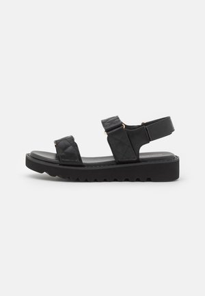 Black platform sandals with quilted straps, open toe, and adjustable ankle strap. Textured rubber sole with zigzag pattern for grip.