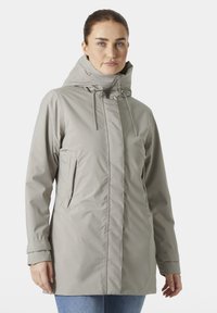 Chaqueta impermeable de color gris claro con un alto cuello, cordones ajustables y bolsillos laterales. Textura suave y diseño de ajuste relajado.