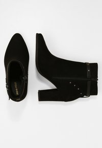 Botines de ante negros con puntera puntiaguda, cremallera lateral y acentos de tachuelas. El diseño del tacón grueso añade estabilidad.