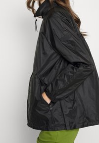 Czarna lekka nylonowa kurtka z wysokim kołnierzem, elastycznymi mankietami, bocznymi kieszeniami oraz regulowanymi sznurkami przy dekolcie.