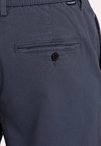 Granatowe spodnie z gładkiego materiału, z tylną kieszenią zapinaną na czarny guzik oraz subtelnymi detalami szycia.