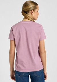 Camiseta de algodón rosa con mangas cortas, un escote redondeado y un ajuste relajado. Detalles de costura visibles en los hombros y el dobladillo.