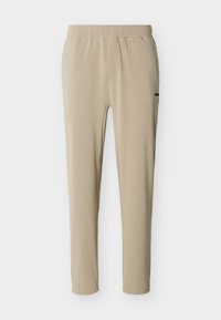 Μπεζ παντελόνια με στενή εφαρμογή, ελαστική μέση και διακριτική καρό υφή, σε απλό λευκό φόντο.