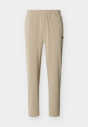Μπεζ παντελόνια με στενή εφαρμογή, ελαστική μέση και διακριτική καρό υφή, σε απλό λευκό φόντο.