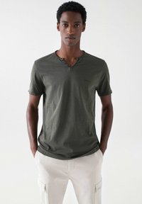 Olivgrünes Kurzarm-T-Shirt mit Henley-Ausschnitt, ausgestattet mit drei Knöpfen am Kragen und einem dezenten Markenlogo auf der Brust.