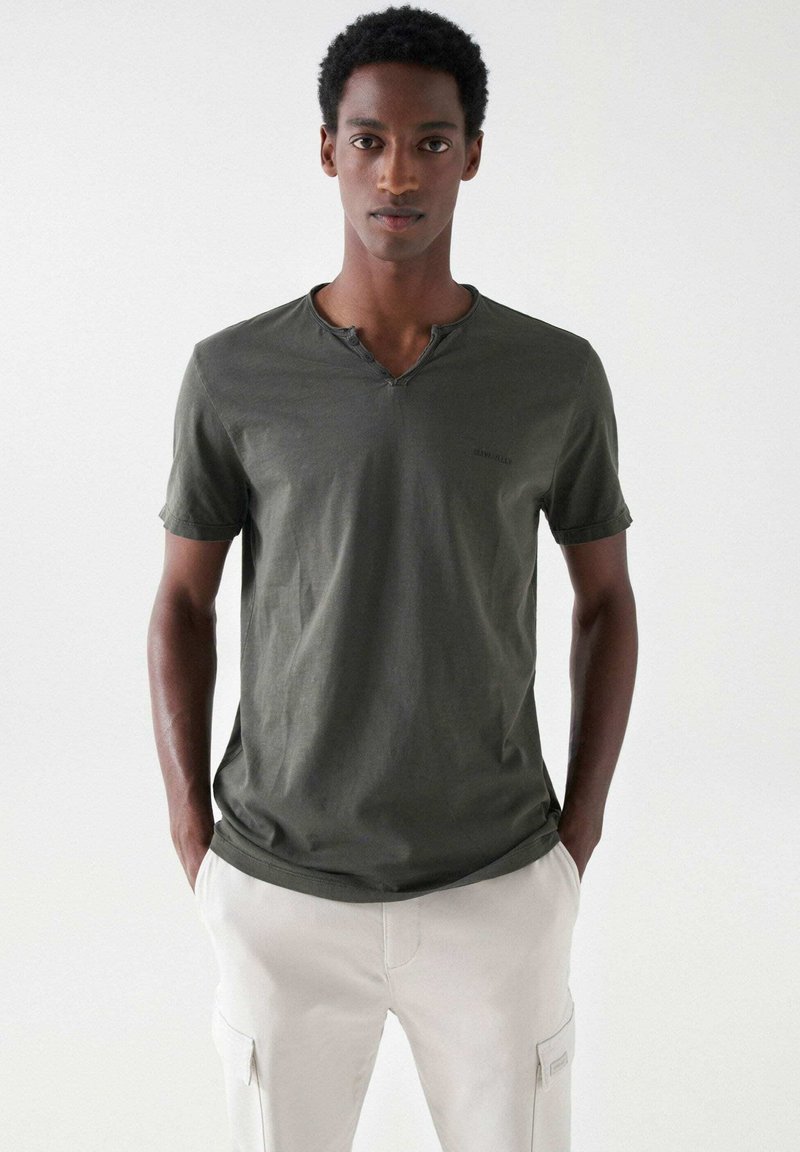 Olivgrünes Kurzarm-T-Shirt mit Henley-Ausschnitt, ausgestattet mit drei Knöpfen am Kragen und einem dezenten Markenlogo auf der Brust.