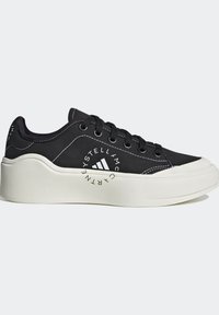 Baskets basses noires avec semelle épaisse blanche, lacets noirs, coutures blanches et logo circulaire Stella McCartney sur le côté.