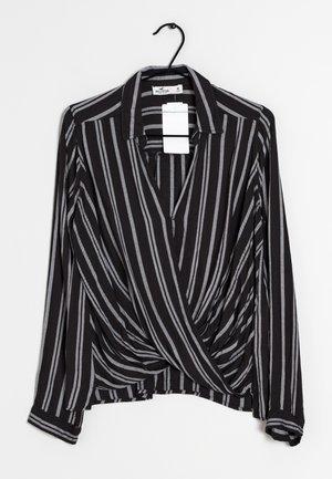 Blouse rayée noire et grise avec un col en V, des manches longues et un design torsadé à l'avant. Le tissu semble léger avec une texture douce.