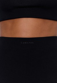 Fekete bordás crop top és leggings szett. Diszkrét márkázással, puha textúrával és testhezálló kialakítással rendelkezik, amely aktív viselethez ideális.