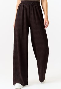 Wide-leg pants in textured dark brown fabric with an elastic waistband, featuring a loose fit that tapers at the ankle. Pairing with white shoes.