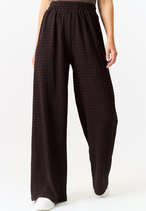 Wide-leg pants in textured dark brown fabric with an elastic waistband, featuring a loose fit that tapers at the ankle. Pairing with white shoes.