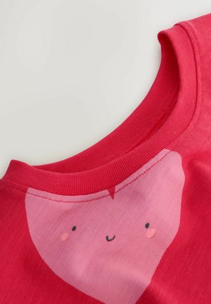 Raudona medvilninė marškinėlių su rožiniu širdelės piešiniu, kuriame yra šypseną turinti veidas. Ribota apykaklė ir minkšta tekstūra su kontrastingos spalvos akcentais.