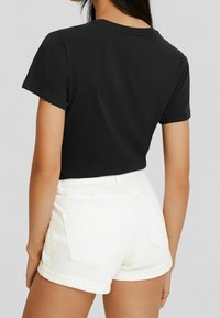 Camiseta negra de manga corta, fabricada en algodón suave, con cuello redondo, combinada con pantalones cortos de denim blanco con puños enrollados y bolsillos traseros.