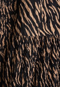 Schwarzer und kastanienbrauner strukturierter Stoff mit einer zerknitterten Oberfläche und einem auffälligen zebraähnlichen Muster, das glatte und raue Texturen kombiniert.