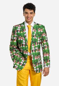 Zelený sako s opakovanou potlačou postáv v zelených oblekoch, kombinované so žltými nohavicami a bielou košou.