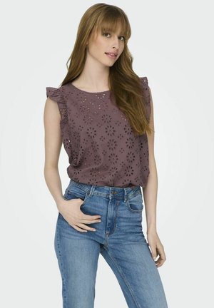 Blouse mauve avec motif à œillets floraux et manches à volant, associée à un jean en denim bleu taille mi-haute. Coupe décontractée, tissu texturé.
