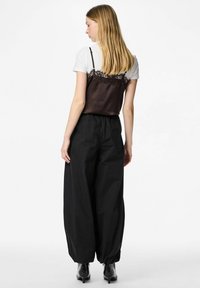 Brūns satīna kamzolis ar mežģīņu apdari, pārģērbts virs baltas T-krekla, saskaņots ar melnām platu kāju biksēm un melniem zābakiem ar augstiem papēžiem. Minimālistisks dizains.