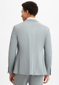 Hellgrauer Blazer mit strukturiertem Finish, tailliertem Design, einer Schlitze hinten und Knopfdetails an den Ärmeln.