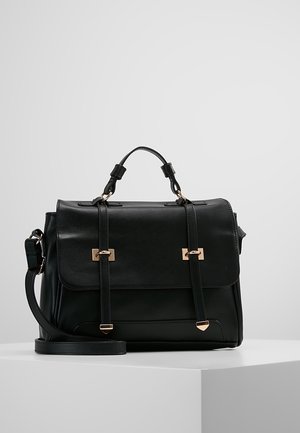 Sac cartable en cuir noir avec poignée supérieure, bandoulière réglable et détails de boucle dorée sur une surface blanche unie.