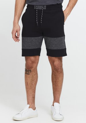 Black and gray fabric shorts with a drawstring waist, featuring contrasting horizontal stripes and side pockets. Worn with white sneakers.