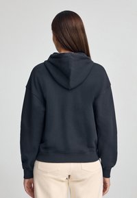 Felpa con cappuccio grigia scura, dal taglio morbido e rilassato, spalle scese e polsini a coste. Presenta una cucitura centrale sul retro e dettagli con tasche.