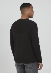 Chemise noire à manches longues en tissu texturé avec un design à panneaux, dotée de manches raglan et d'un col arrondi, vue de l'arrière.