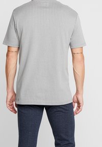 Grå ribbad t-shirt med kort ärm och rund hals, med en mjuk textur och rak nederkant, sedd bakifrån.