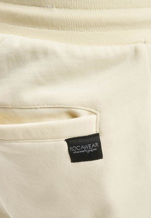 Krämfärgade sweatpants med texturerad midja, som har en sidficka och en svart RocaWear-etikett. Mjukt, avslappnat material.
